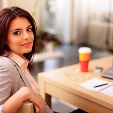 Young businesswoman sitting at desk and working. Smiling and looking b