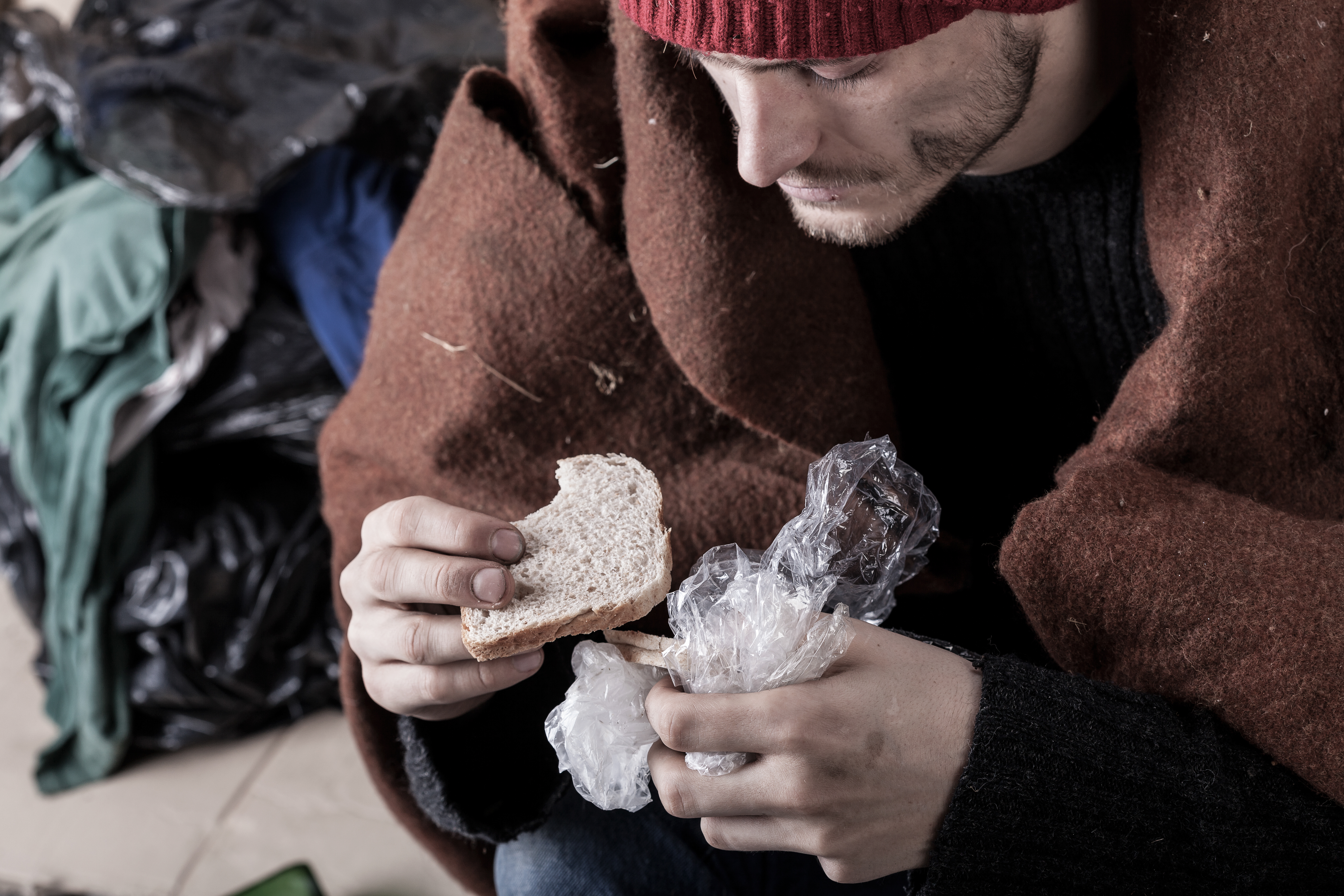 Poor man eating sandwich on the street.
